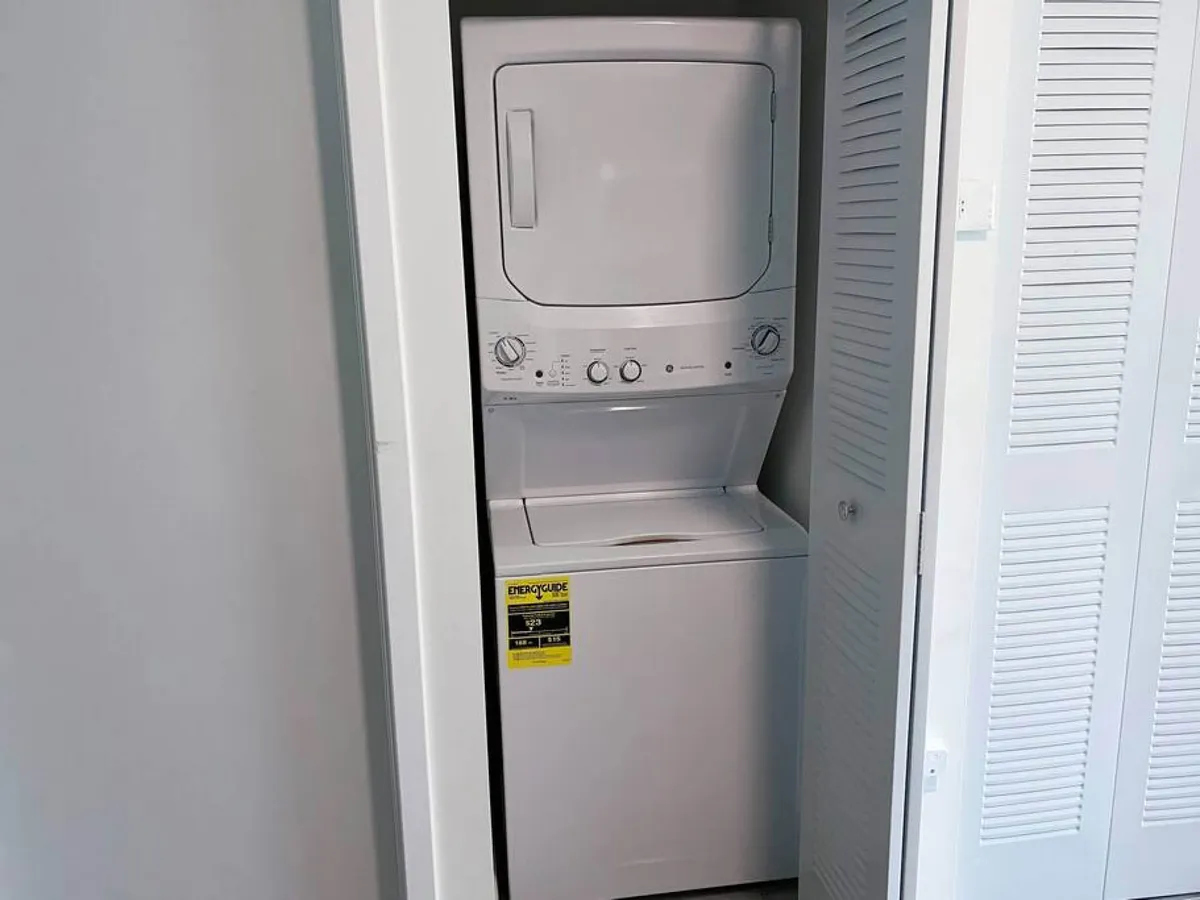 A stacked washer and dryer is neatly tucked into a dedicated laundry closet, with shelves above for laundry essentials. The space is clean, bright, and designed for easy access, emphasizing the practicality of having in-unit laundry.