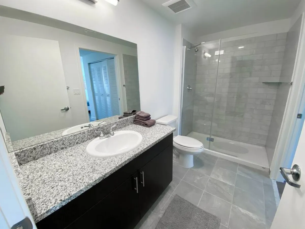 This image showcases a modern bathroom interior featuring a large mirror above a granite countertop sink, a glass-enclosed shower area, and a toilet situated next to the shower. The space appears clean and thoughtfully designed, exuding a calm and refreshing mood.